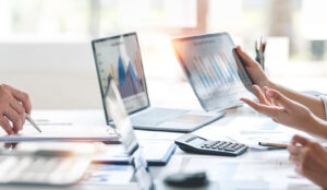 An image showing a close-up of business professionals analyzing data charts on a digital tablet and laptop during a meeting.